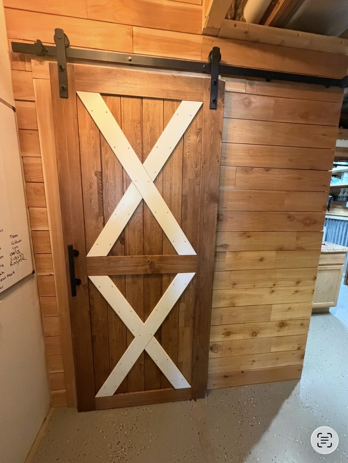 After - custom wood sliding barn door with white X-bracing and black hardware installed on wood plank wall