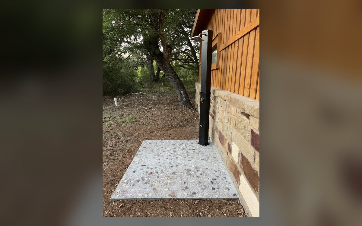 After - outdoor solar shower on pebble concrete pad beside Hill Country home