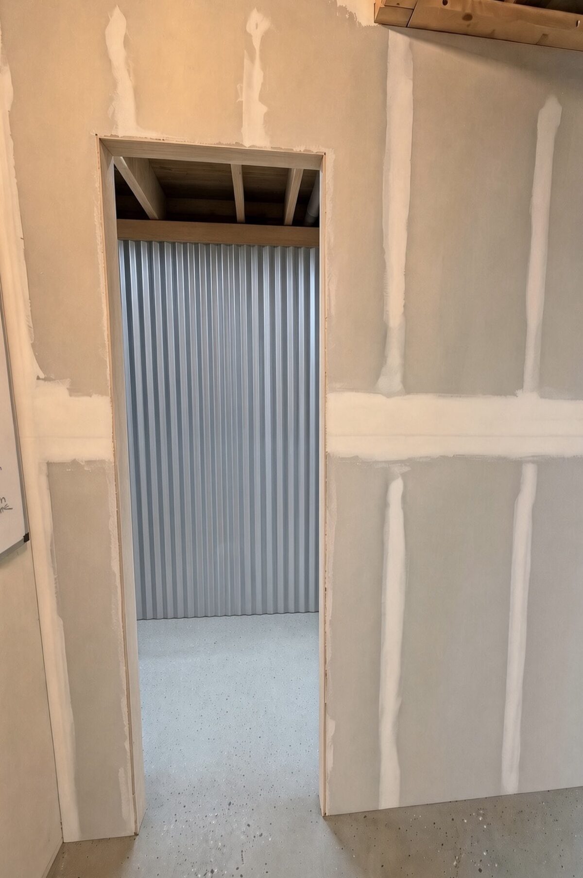Before - open unfinished doorway with drywall mud and corrugated metal wall beyond